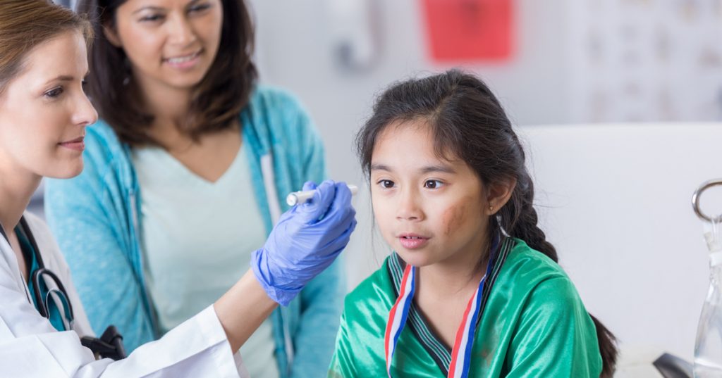 Female emergency room doctor uses a pen light to examine a young soccer player's eyes